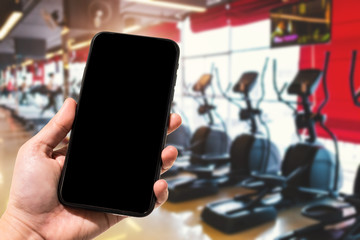 Close-up of female use Hand holding smartphone blurred images touch of Abstract blur of defocused sport gym interior and fitness health club with sports exercise equipment Gym blur background.