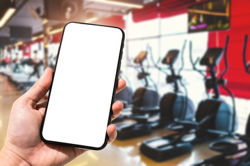 Close-up of female use Hand holding smartphone blurred images touch of Abstract blur of defocused sport gym interior and fitness health club with sports exercise equipment Gym blur background.