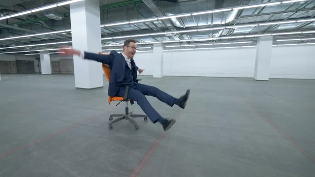 Man in a suit is fooling around while sitting in a rolling chair
