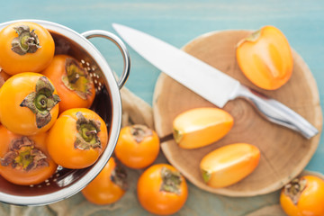selective focus of orange persimmons in colander and slices on cutting board with knife