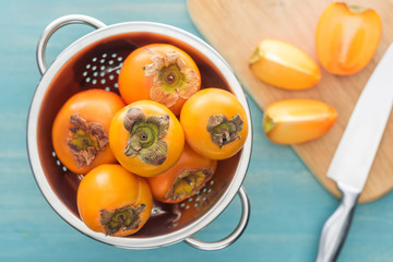 selective focus of persimmons in colander and slices on cutting board with knife
