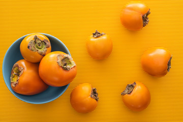 top view of orange persimmons on blue plate on yellow background