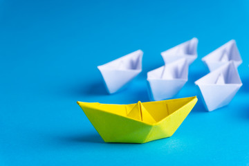 White and yellow paper boat or ship in one direction on blue background. Business for innovative solution concept with selective focus