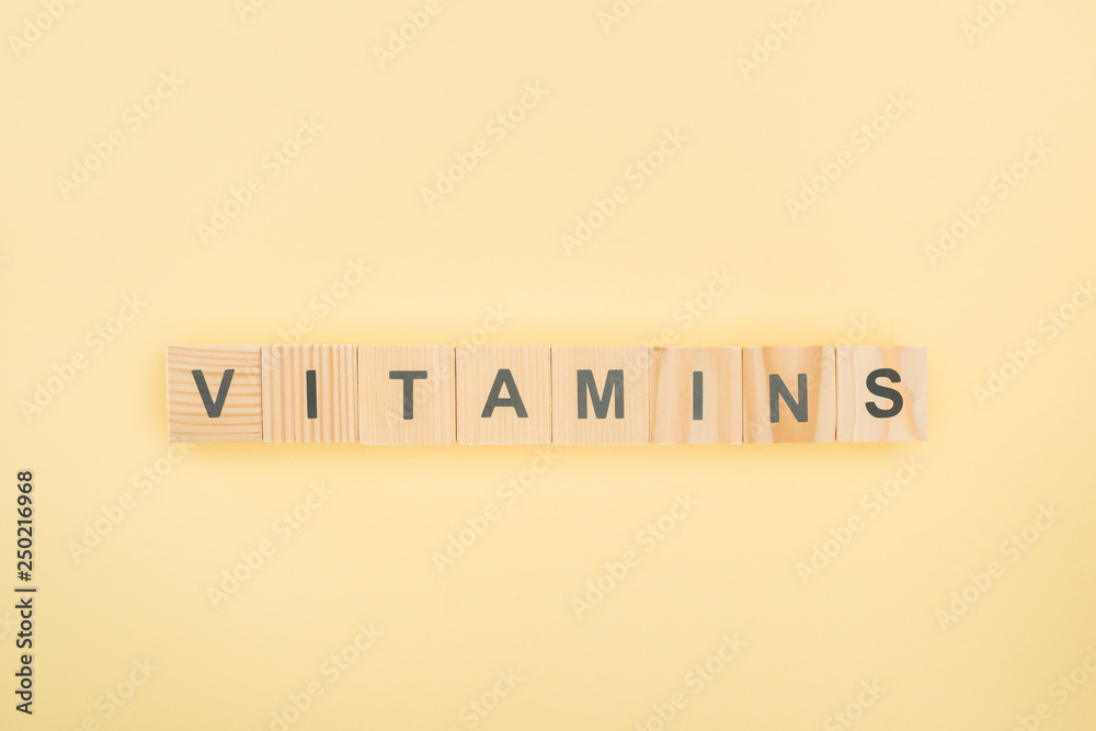 Wall mural top view of vitamins lettering made of wooden cubes on yellow background - Wall murals