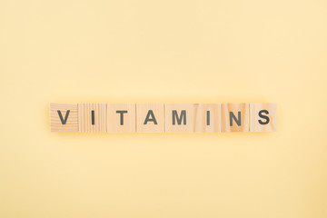 top view of vitamins lettering made of wooden cubes on yellow background