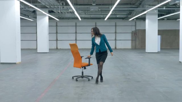A woman in office clothes is happily wheeling a rolling chair along the hall