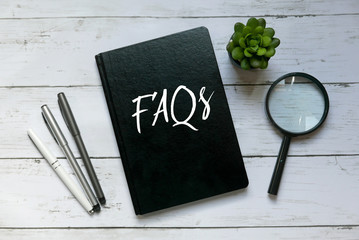 Top view of pen,magnifying glass,plant and book written with FAQs on wooden background.