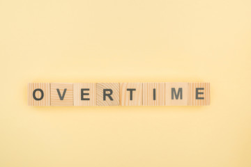top view of overtime lettering made of wooden cubes on yellow background