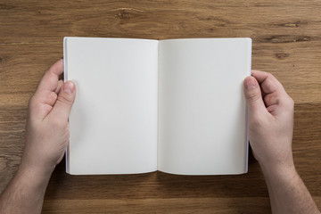 Obraz premium Hand holding white blank paper sheet mockup on wooden background