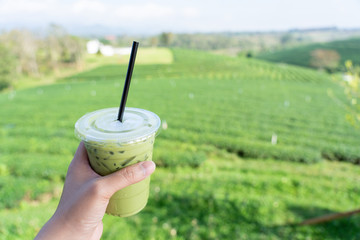 Young man hand holding a glass of green tea drink Filed with a large tea plantation background Green tea is a healthy drink Useful to the body