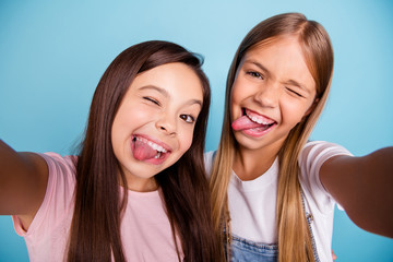 Close up photo two pretty little age girls holiday having fun funky tongue out of mouth make take selfies long pretty hair wearing casual jeans denim t-shirts isolated on blue bright background