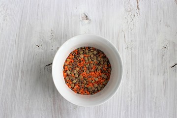 Orange and brown lentils in a clay white bowl on a white wooden background