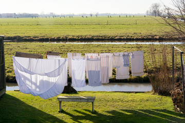Clean clothes drying in the wind on a washing line on a beautiful sunny day in spring. Situated in a beautiful typical Dutch flat landscape with grassland, ditches and willows.