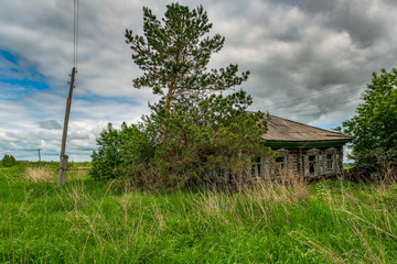 Old dilapidated wooden house in an abandoned village on a cloudy sky background. The ruins of a wooden hut on a grassy street