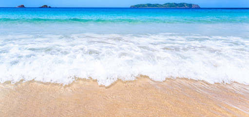 Beautiful amazing gold colored sandy beach with soft waves isolated with sunny blue sky. Concept of tropical calm tourism idea, copy space, close up