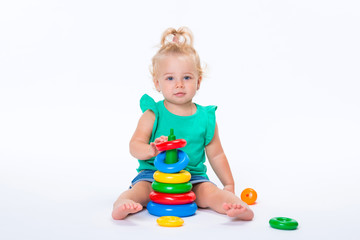 Cute kid blonde girl playing with color pyramid toy isolated on white background. Happy childhood and pre-school development of children