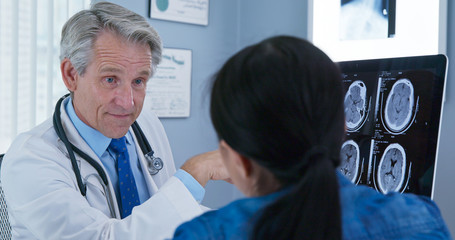 Obraz premium Primary care doctor talking to patient about test results from specialist on his computer. Senior Caucasian male physician explaining brain scans to woman