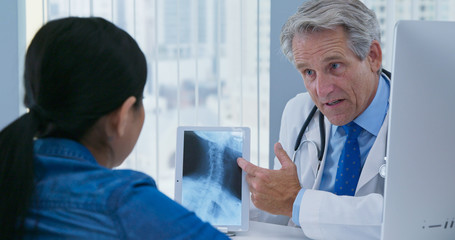 Radiologist or doctor talking to woman about spinal injury using tablet computer screen with x-ray. Physician and patient having conversation with xray in office