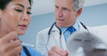 Fototapeta premium Primary care physician talking to surgeon about patient recovery. Medical professionals consulting together on paperwork. Senior Caucasian male doctor and female Japanese nurse