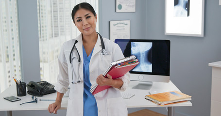 Portrait of Japanese woman doctor standing at her desk looking at camera. Medium shot of confident...