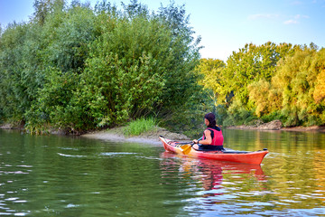 Woman paddle red kayak. Kayaking near overgrown shore of green thick at river at summer. Concept for adventure, travel, action, lifestyle.