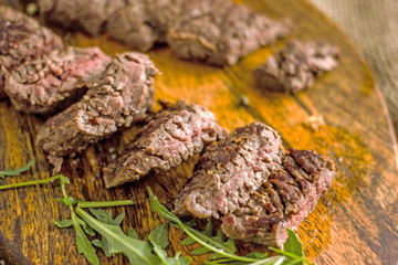 Beef Machete Steak. Grilled steak on a wooden board on a dark background. Delicious grilled meat, medium steak grilled, roast beef pieces.  Machete steaks of medium roast on a wooden board