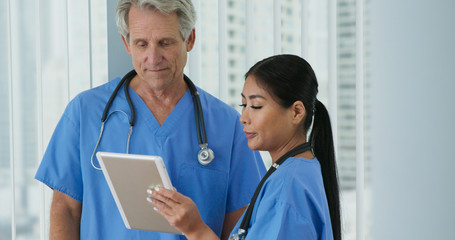 Two friendly medical professionals working together on tablet computer. Medium shot of Japanese woman doctor and Caucasian male nurse going over digital paperwork in hospital