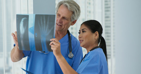 Obraz premium Two doctors looking over x-rays of wrist together in hospital. Medical professionals looking at broken bones to determine course of care. Senior man and adult woman