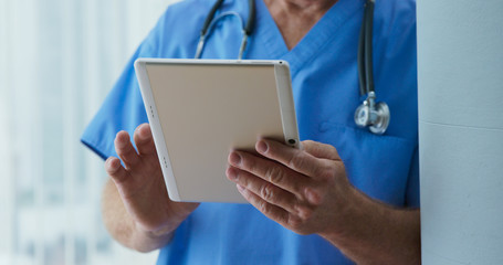 Close up on Senior Caucasian male doctor to tablet computer as he reads medical history of patient. Older man medical professional looking over records on pad