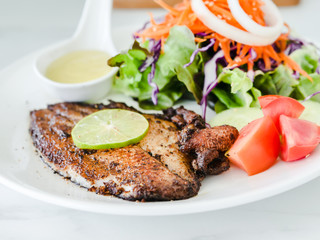 Grilled fish steak with salad with white plate on marble table.