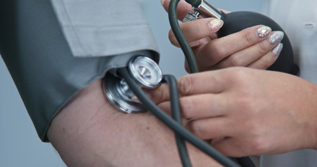 Extreme close up on stethoscope and blood pressure cuff on arm as doctor checks older male patient. Rack focus to pumping bulb to inflate sphygmomanometer