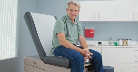 Portrait of Senior Caucasian male patient sitting on exam room table looking at camera. Older man in hospital for regular check up