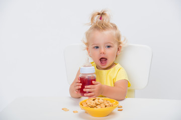Cute little baby girl 1 year old eating cereal flakes and drinking juice or compote from a bottle...