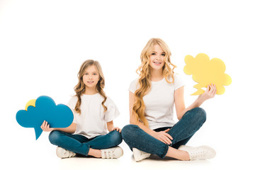 smiling mother and daughter sitting in floor with crossed legs and holding speech bubbles on white...