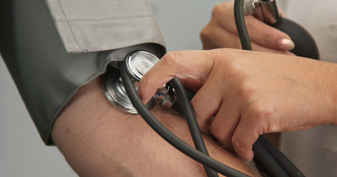 Extreme close up on stethoscope and blood pressure cuff on arm as doctor checks older male patient using sphygmomanometer
