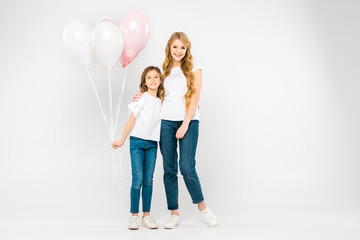 Fototapeta premium happy mother hugging adorable daughter holding air balloons on white background