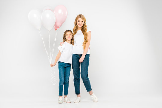 happy mother hugging adorable daughter holding air balloons on white background