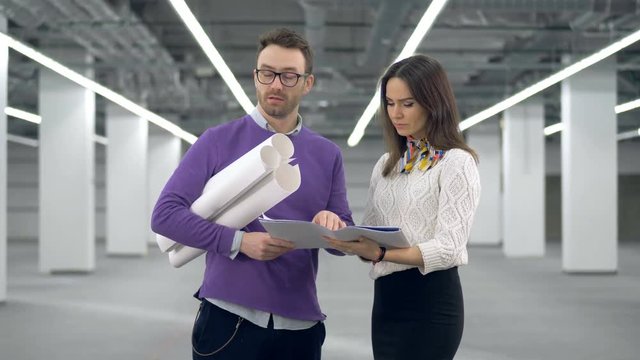 Male architect is holding drawings and talking to his female colleague