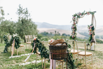 Floral garlands of green eucalyptus and pink flowers decorate wedding arch and chairs on the hill