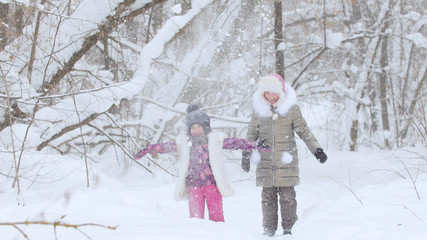 Two little girls playing with snow in winter forest. Throwing the snow in the air