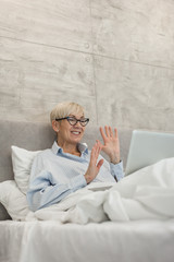 Senior woman with glasses using laptop in bed