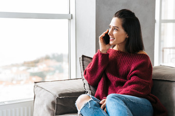 Woman indoors in home on sofa talking by mobile phone.
