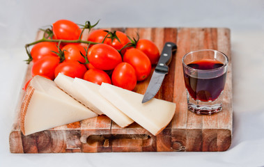 wooden chopping board with cherry tomatoes, cheese and a glass of red wine