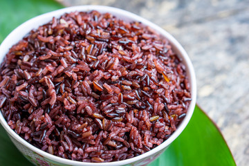 cooked purple rice berry in bowl over green leaf background on wooden table closeup, healthy eating food concept 