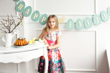 Attractive little girl in a colorful dress posing and smiling against the background of a decorated Easter cake and eggs