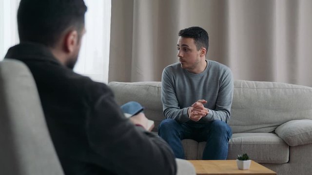 Male psychoanalyst listening patient and writing notes in psychologist office