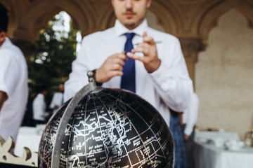 Man in the suit stands before the black globe with silver letterings