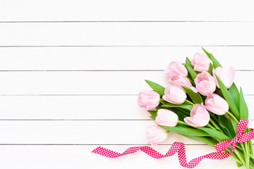 Bouquet of pink tulips decorated with ribbon on white background. Top view, copy space. Greeting card.