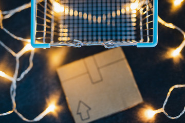 shopping cart with cardboard parcel on concrete desk surrounded by fairy lights