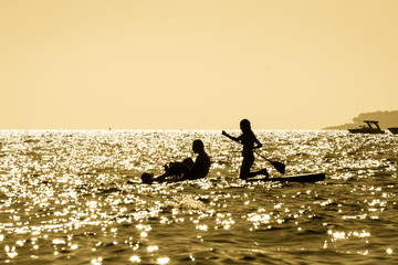 Silhouette of a young couple paddling on a surf at sunset in Maro, Andalusia, Spain.
